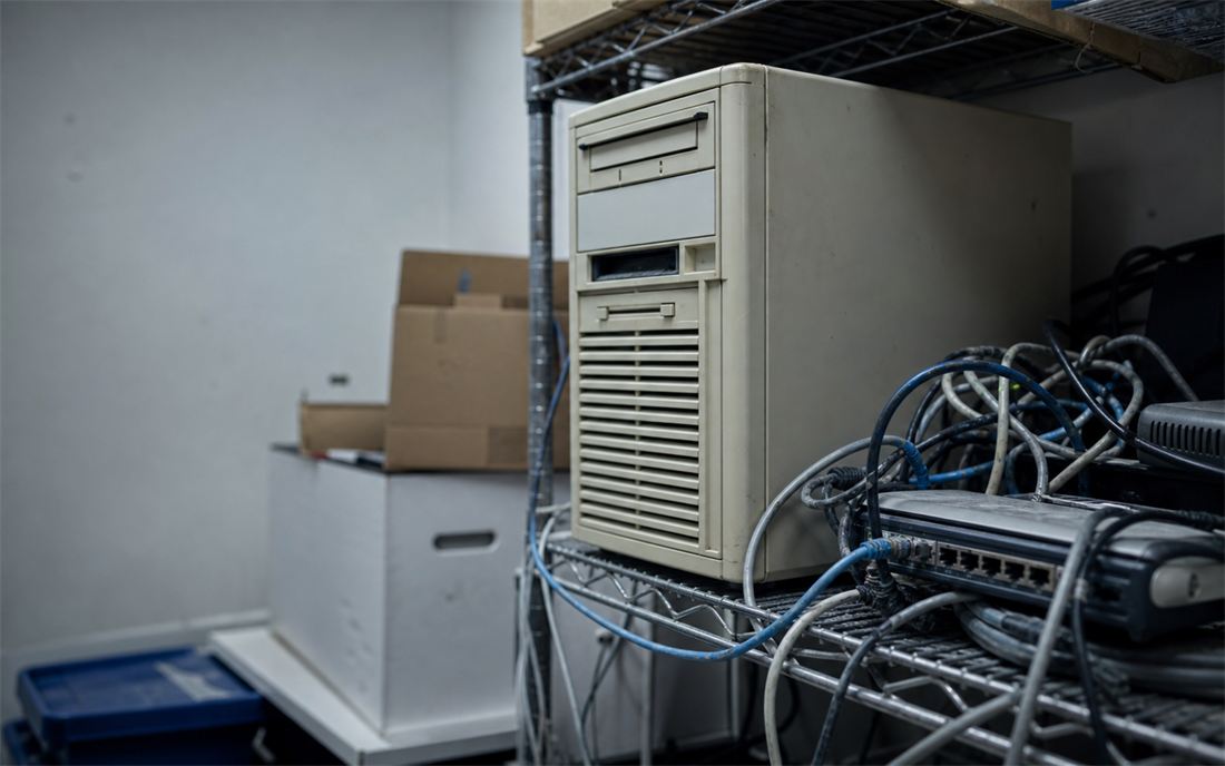 Aging tower server and tangled network cables on a wire rack in an office closet